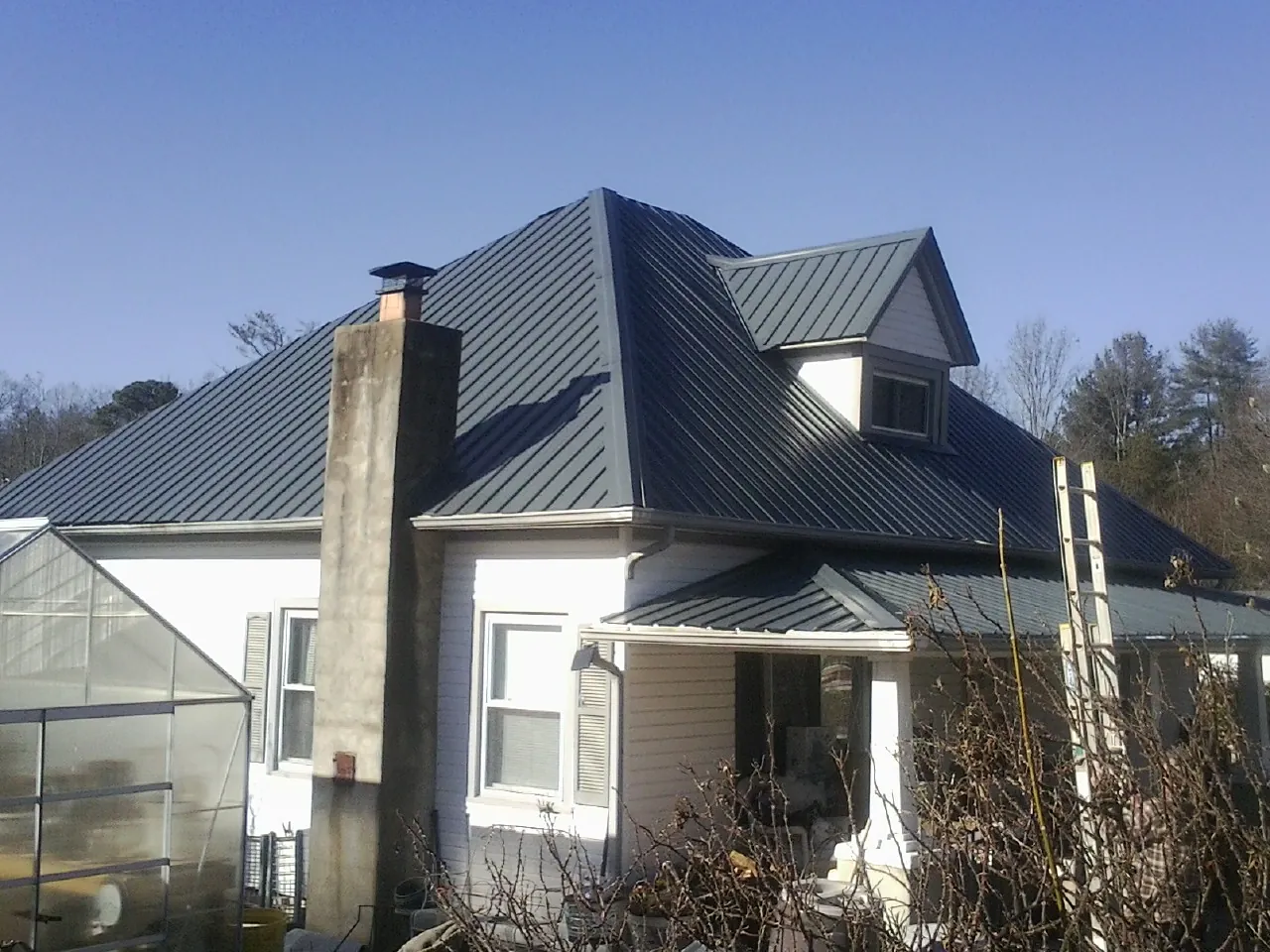 Dark blue standing seam metal roof on a white farmhouse with dormer — Slate & Tile Roof Repair by Roofing Brothers in Bridge City