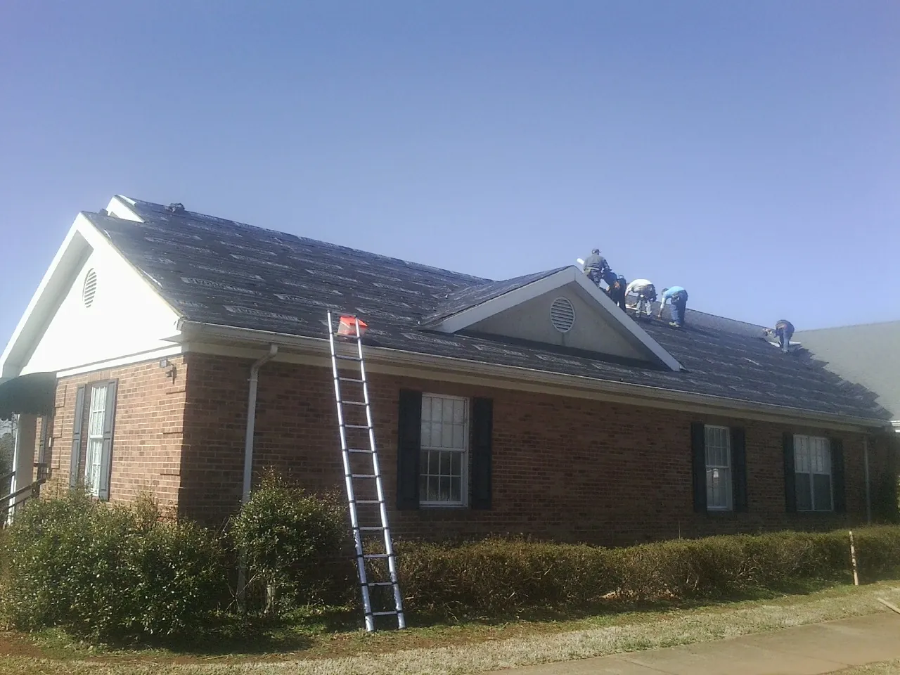 Crew tearing shingles off a brick ranch roof with a ladder set — Emergency Roof Repair work by our crew in Bridge City