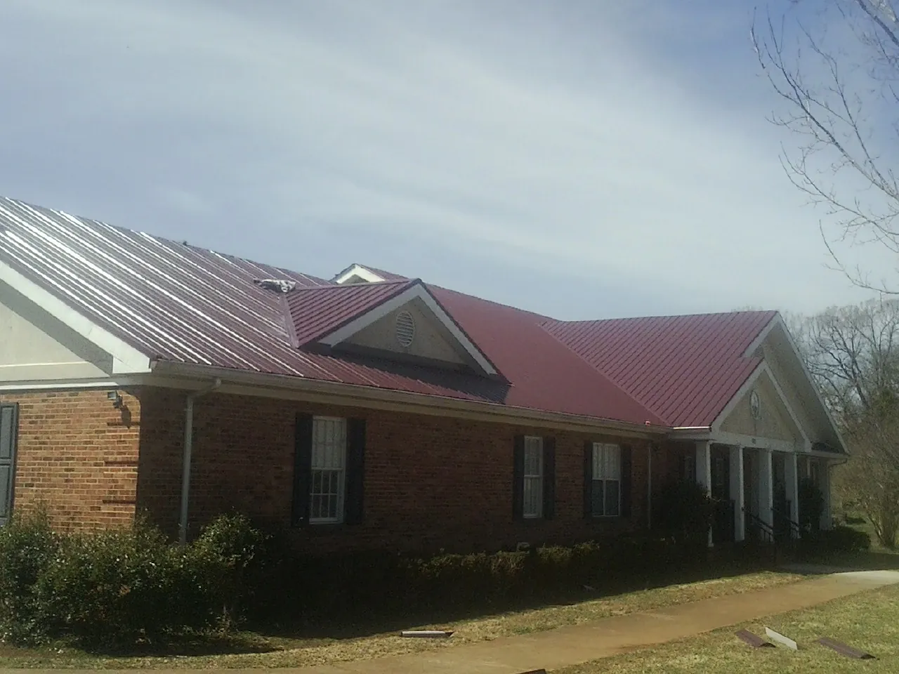 Red metal roof with gabled entries on a long brick building, from a Hail Damage Roof Repair job in Bridge City