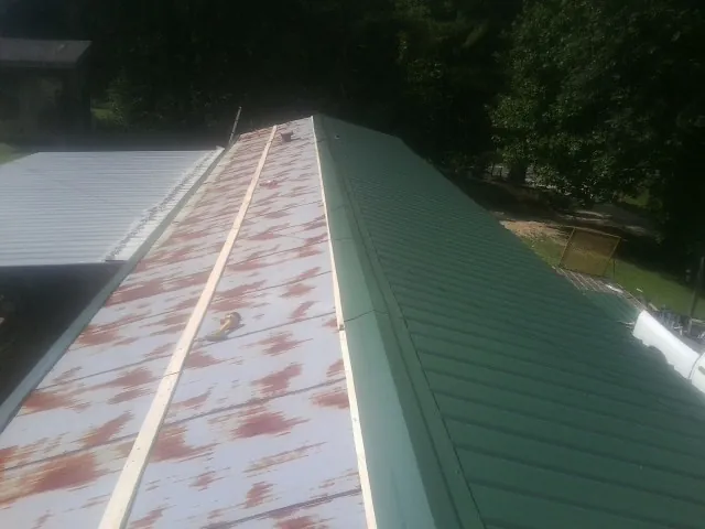 Old rusted panels beside newly installed green metal roofing — Wind Damage Roof Repair by Roofing Brothers in Bridge City