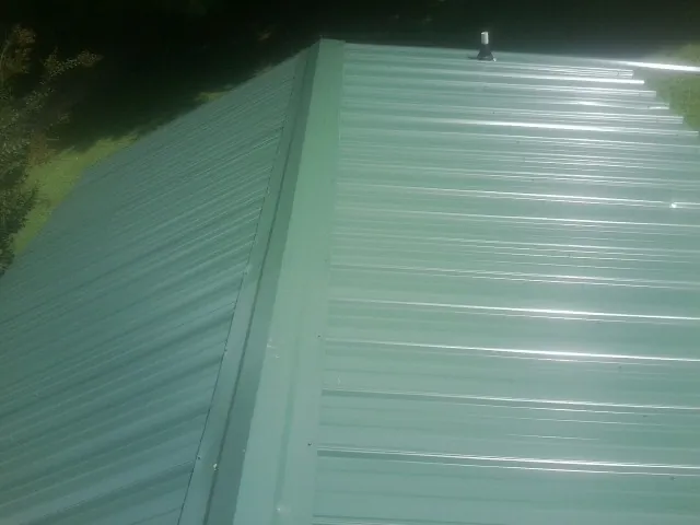 New green metal panels meeting at the ridge of a roof — Flat Roof Repair work by our crew in Bridge City