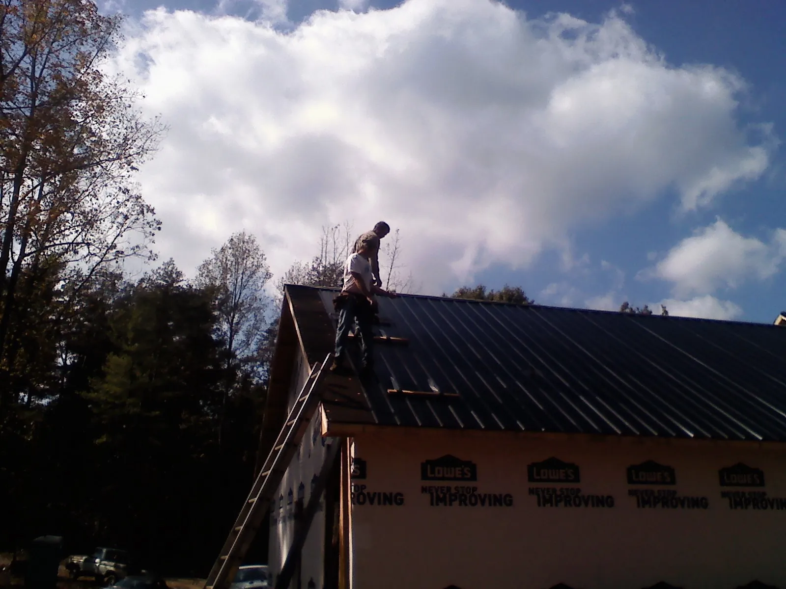 Roofer fastening dark metal panels high against a cloudy sky, from a Roof Inspection job in Bridge City