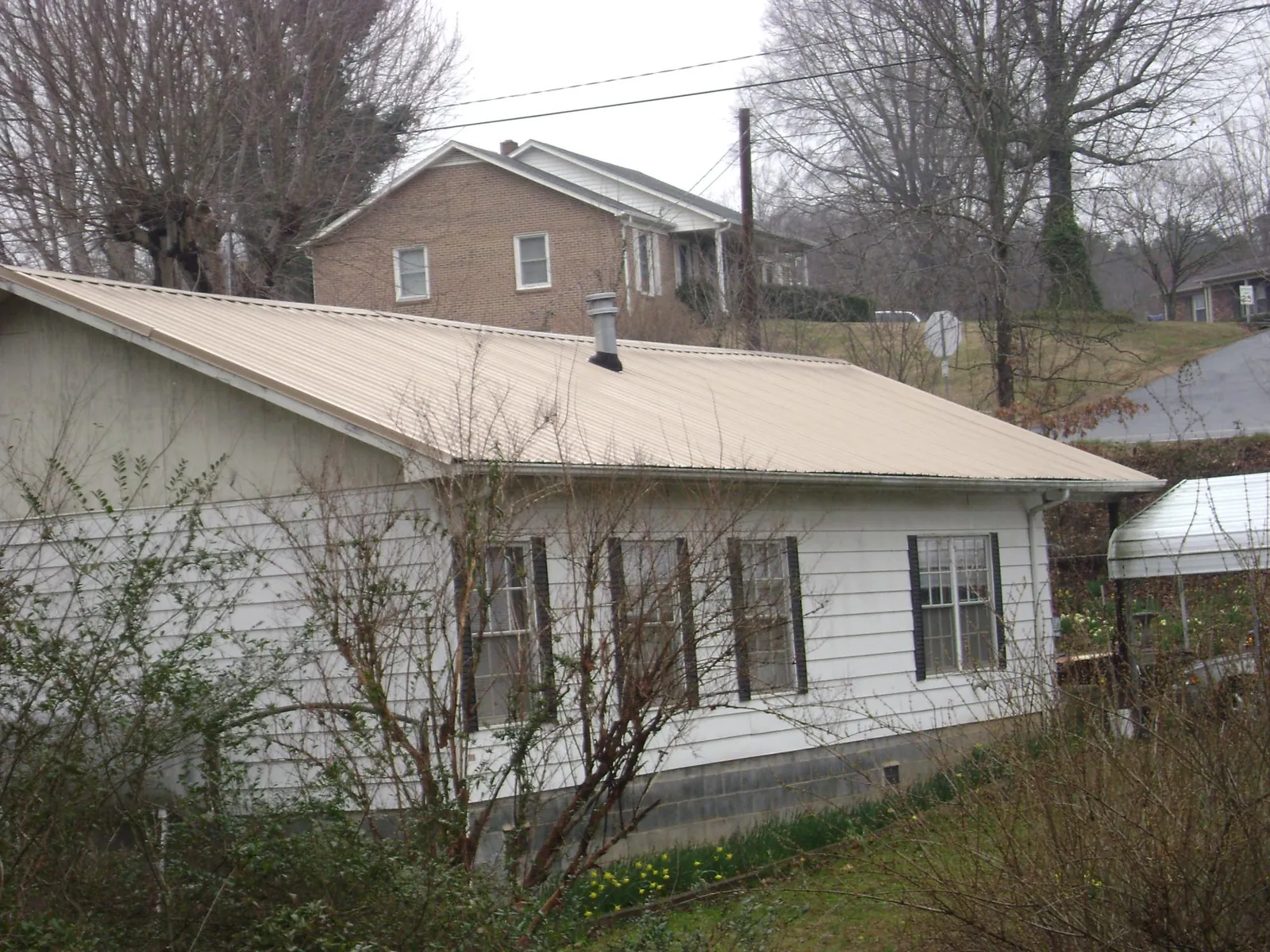 Tan metal roof on a white sided house set into a hillside — Commercial Roofing by Roofing Brothers in Bridge City