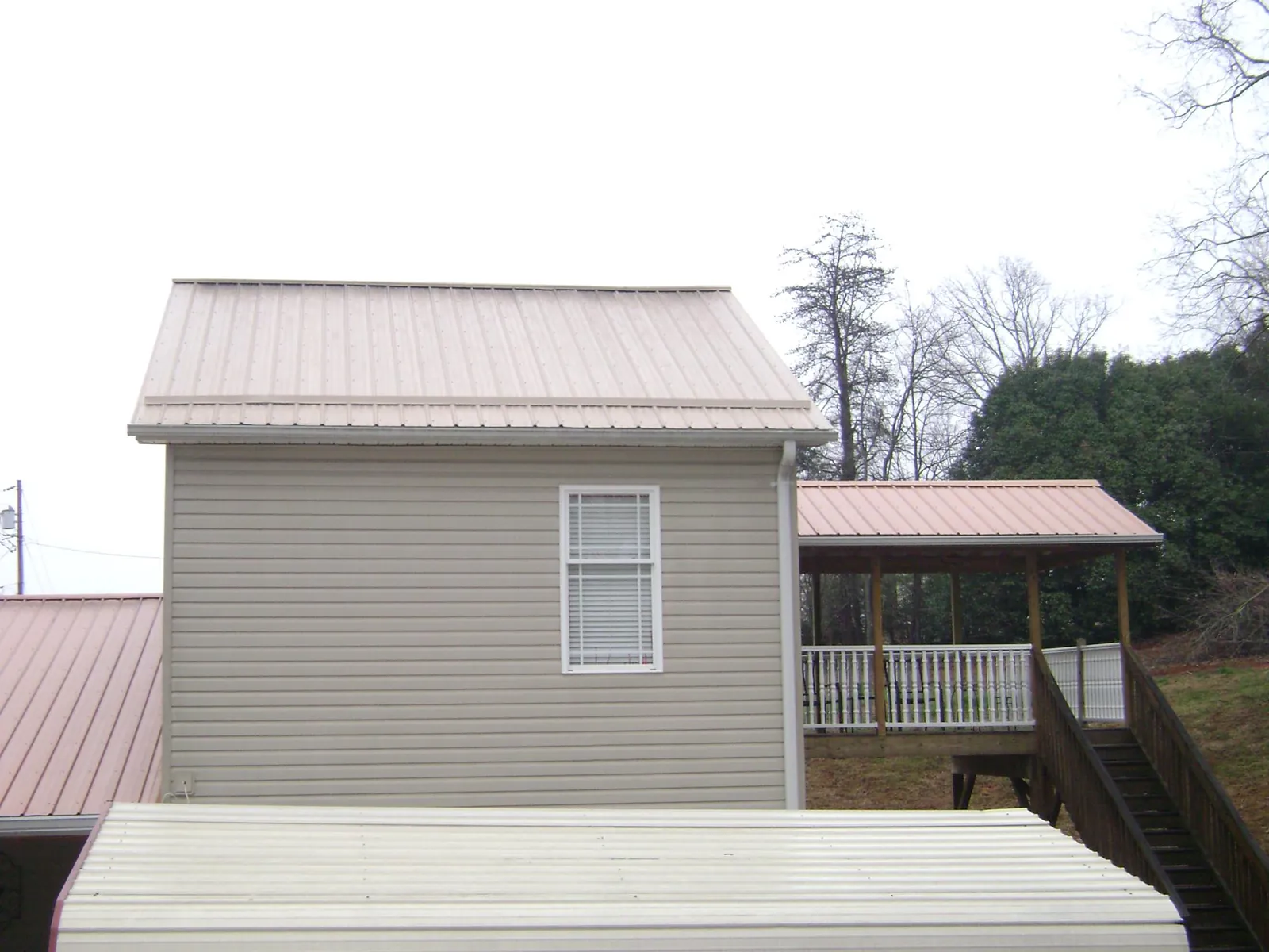Tan metal roofs on a two story addition and attached porch, from a Roof Replacement job in Bridge City